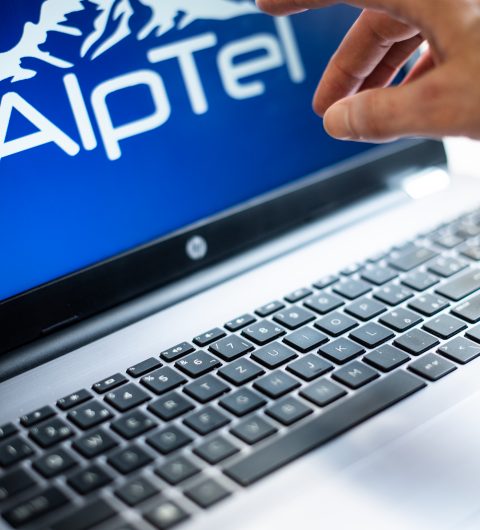 Hand tippt auf Laptop mit Alptel Logo